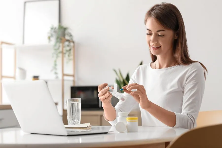 A woman sits at her desk and smiles at the different supplements she is holding.